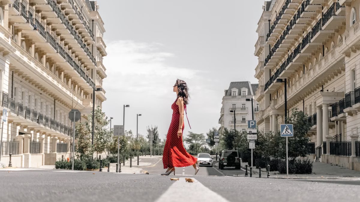 A fashionable woman in a red dress walks between elegant buildings in Baku, Azerbaijan.
